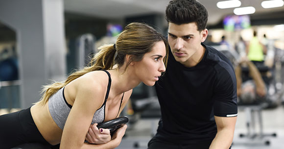 Personal Trainer mit einem Kunden in einem Fitnessstudio bei der Durchführung von Übungen.